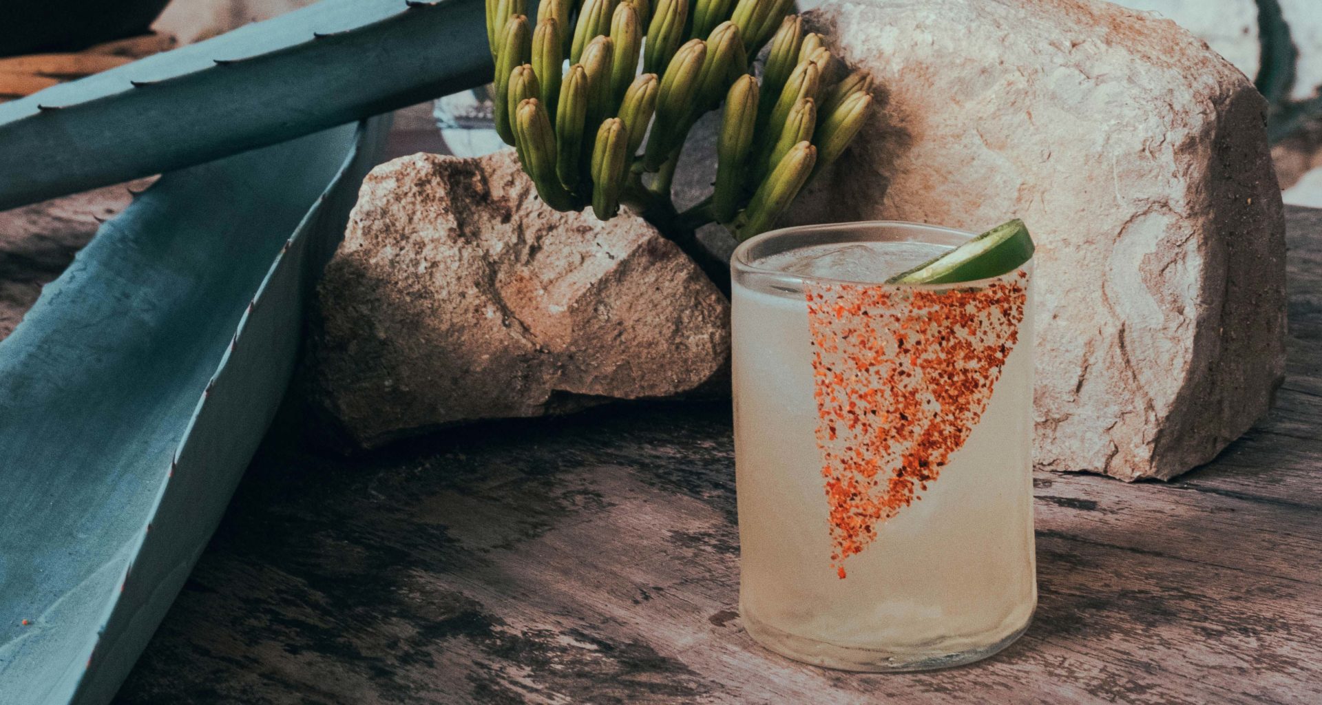 Cocktail de jalapeño con fondo de maguey y piedras sobre una mesa de madera